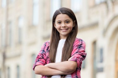 Şık ve kendinden emin. Kendine güvenen çocuk kollarını açık havada çapraz tutuyor. Şirin bir kızın moda görünüşü. Sıradan bir tarz. Modayı takip eden çocuklar giyer. Çocuk kıyafetleri. Kendine güven sana çok yakıştı.