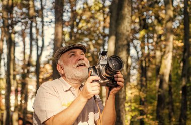 Retro kamera. Anı yakala. Emeklilik ve emeklilik. Eski fotoğraf makineli adam fotoğrafçısının klasik stil fotoğrafı. Sonbahar doğa geçmişi. Gülümse. Kamerayı tutan bir turist. Ormanda güzel bir hafta sonu.