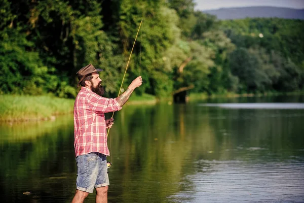 Che pesce! uomo barbuto maturo con pesce su asta. pesca d'altura. rilassarsi sulla natura. pesca hipster con cucchiaio-esca. pescatore di successo in acqua di lago. hobby del pesce della mosca. Attività estive — Foto Stock