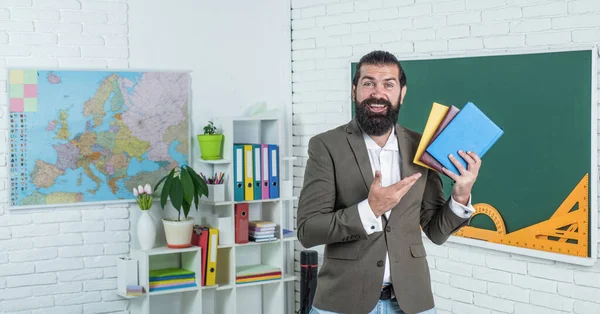 Motivo della formazione. Torniamo a scuola. educazione informale. felice insegnante maturo che mostra i libri dalla biblioteca. l'uomo barbuto lavora in classe con cartella di lavoro. prepararsi per l'esame. docente universitario sulla lezione — Foto Stock