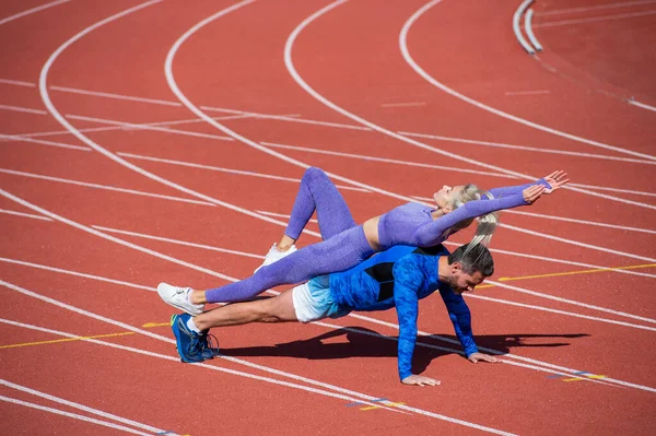 Spor fitness erkek ve kadın antrenmanları birlikte kalas oluşturun ve açık stadyum yarış pistinde spor kıyafetleri ve spor antrenmanları giyerek şınav çekin. — Stok fotoğraf