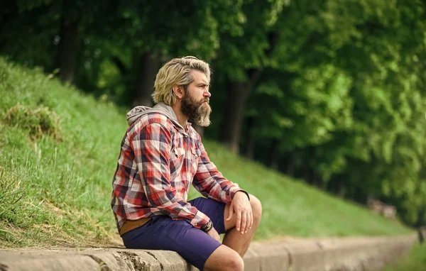 Omtänksam hipster sitta i parken. njuta av naturen i vår. manligt mode. Han bär ledigt. brutal hipster med långt skägg och färgat hår. mogen student koppla av utomhus. Vila dig. — Stockfoto