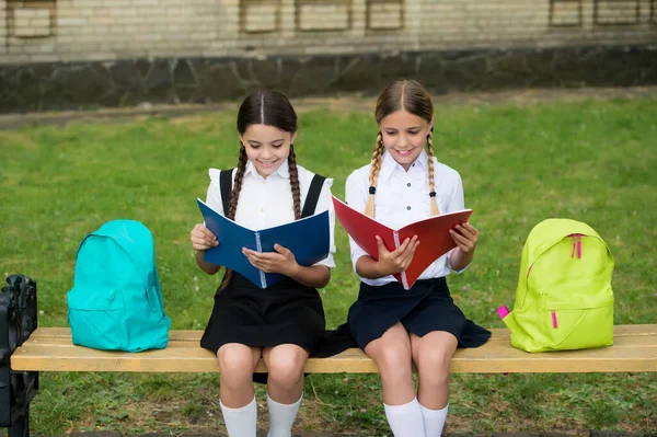 Crianças em uniformes escolares lêem livros de biblioteca sentados no banco ao ar livre, lendo — Fotografia de Stock