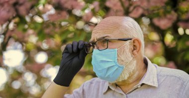 Virüs enfeksiyonundan koru. Enfeksiyonun yayılma riskini sınırla. Enfeksiyon havada. Son sınıflar covid-19 hakkındaki yanlış bilgilere inanıyorlar. Dışarıda maske ve eldiven takan kıdemli bir adam var.