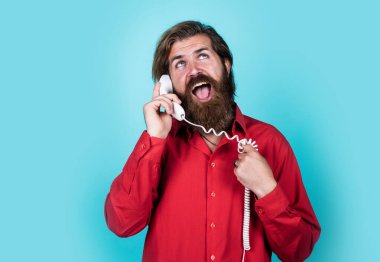 İletişim konsepti. Gömlekli sakallı adam telefonda. Sohbet sırasında sıradan bir adam. Uzun saçlı ve bıyıklı duygusal hippi. Erkek retro telefondan konuşuyor.