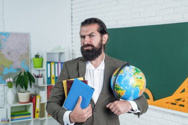Kostümlü olgun sakallı adam öğretmen. Okulda coğrafya haritası ve seyahat ile birlikte otur.
