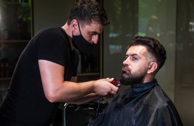 Sihirli bakış. Profesyonel berber ustası olan acımasız adam elektrikli tıraş makinesi kullanıyor. Hipster. Erkek berber bakımı. Kuaför salonundaki sakallı adam. Güzellik ve moda. saç ve sakal şekillendirme