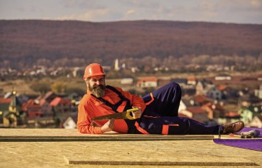 İnşaatçı testeresi. Profesyonel tamir çatısı. Düz çatı kurulumu. Özel koruma giysisi içinde çatı tamircisi. İnşaat binasının altındaki yeni çatı
