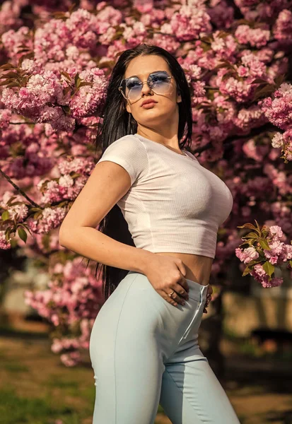 Seksi kız parktaki kiraz çiçeklerine bakıyor. Seksi kız sakura çiçeğinin tadını çıkarıyor. Kiraz çiçekli kadın. Güneşli bir günde çiçek açan ağaç. Bahçesinde bahar çiçekleri olan genç bir kadın. Güzel Yaz mankeni kız — Stok fotoğraf