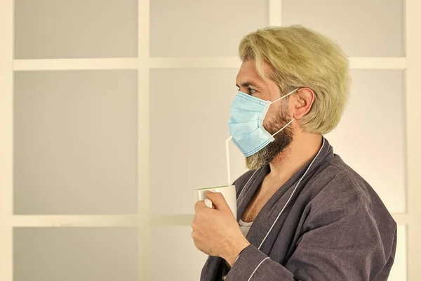 Пандемічний карантин. Антивірусна маска. Маски для захисту від вірусу. Чоловік носить маску для захисту від вірусних інфекцій. чоловік п'є каву в медичній масці. ранок вдома на самоізоляції коронавірусу — стокове фото