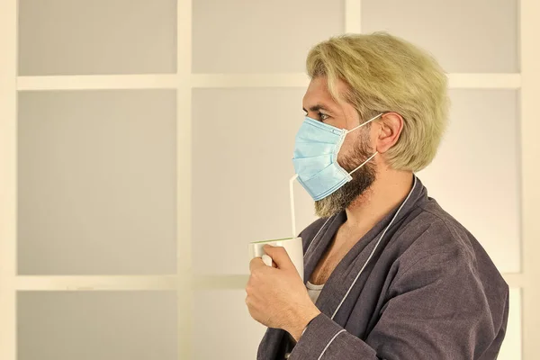 Pandemische quarantaine. Anti-virus masker. Maskers om te beschermen tegen virussen. De man draagt een masker om zich te beschermen tegen virale infectie. De man drinkt koffie met een medisch masker. ochtend thuis op coronavirus zelfisolatie — Stockfoto