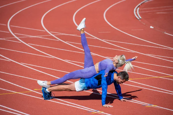 Spor fitness çiftleri birlikte antrenman yapıyor kalas gibi ayakta duruyor ve spor kıyafetleri, spor kıyafetleri ve fitness giyerek stadyum yarış pistinde şınav çekiyorlar. — Stok fotoğraf