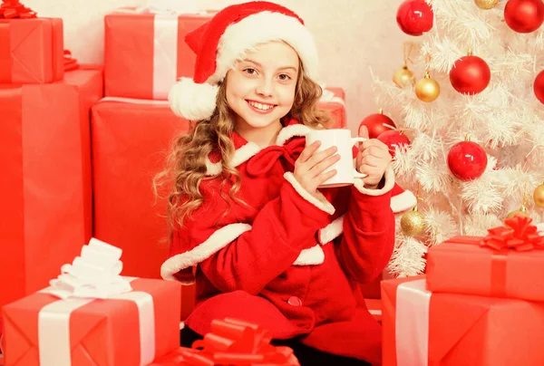 Kid Santa hatt njuta av kakao dryck. Perfekt sätt att värma dig semesterperioden. Flicka lilla söta barn hålla mugg med varm dryck medan fira jul. Varm choklad på julafton. Kakaofavoritdryck — Stockfoto