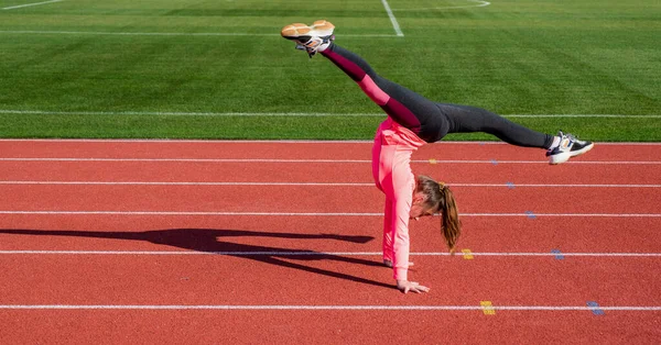 Träning på frisk luft. säker gymnast med flexibel kropp. Gymnastik. Tonårstjej gör trick på stadion. Killen i sportkläder. barn gör kupper motion på racing spår. hälsosam barndom. Energi inuti — Stockfoto