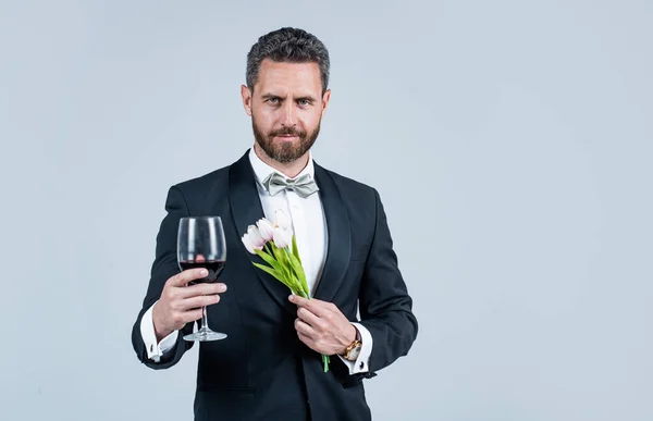 Stilig smoking man i fluga med blomma bukett hälsning med glas rött vin, glad Alla hjärtans dag, kopiera utrymme — Stockfoto