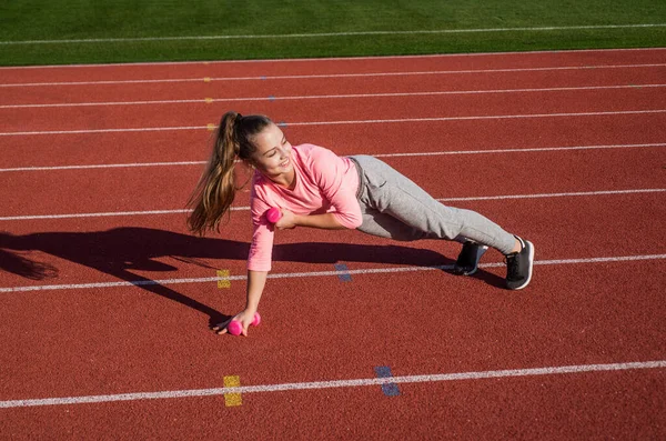 Poder y equilibrio. una infancia saludable. entrenamiento al aire libre. atleta seguro de sí mismo con barra. adolescente chica calentando en el estadio. Un chico en ropa deportiva usa mancuerna. niño hacer ejercicio en pista de carreras — Foto de Stock