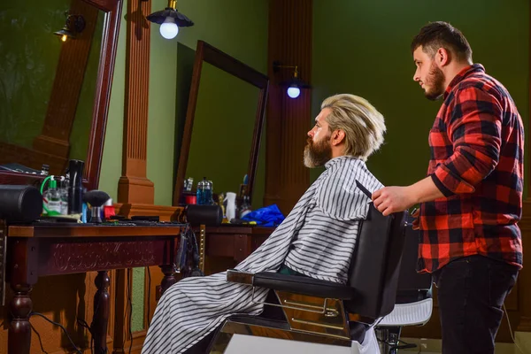 El hombre quiere un peinado nuevo. belleza masculina y la moda. un hombre maduro en la barbería. hombre barbudo brutal en la peluquería. peluquero profesional con cliente masculino. hipster con barba teñida y bigote — Foto de Stock