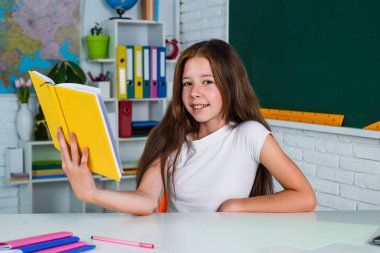 Kara tahtanın yanında elinde kitapla tatlı bir çocuk okula geri dönüyor.
