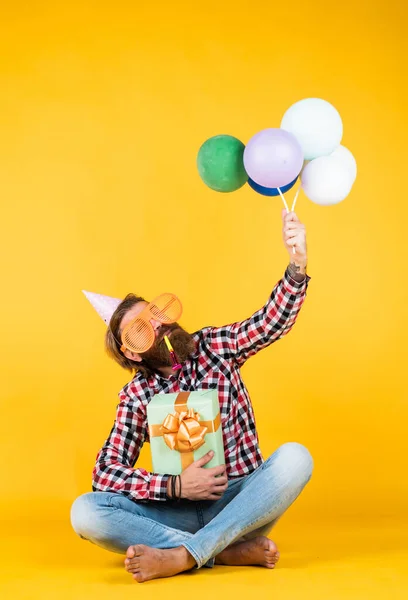 Branco hipster maduro com óculos de festa engraçados em camisa quadriculada segurando balões e caixa de presente, celebração — Fotografia de Stock