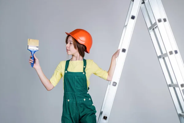 Professionista intelligente. costruzione e ristrutturazione. costruzione di bambini. ingegnere adolescente è lavoratore edile. giornata internazionale dei lavoratori. pittore sulla scala a pioli. ragazza in casco giochi costruttore — Foto Stock