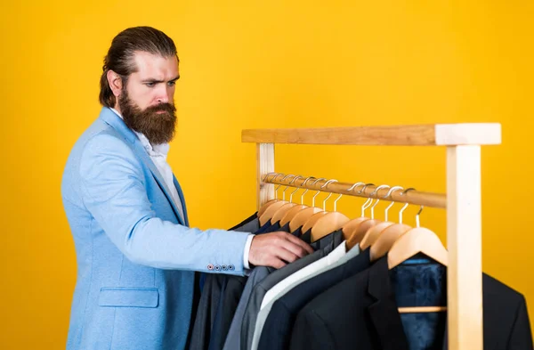 Goed verzorgd man in bruiloft formalwear heeft baard kiezen jas in garderobe, mode — Stockfoto