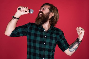 Müzikle yüzleş. Bıyıklı vahşi yakışıklı adam şarkı söylüyor. Olgun adam mikrofonda şarkı söylüyor. Karaoke. Sıradan moda stili şarkıcı. modern görünümlü sakallı hippi mikrofonlu.