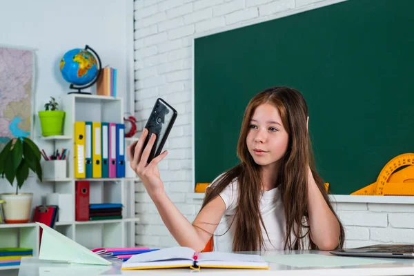 做自拍。女孩是大学生。回学校去十几岁的女孩在教室里用智能手机工作。快乐的孩子在网上学习。现代教育。知识日。有电话的小学生 — 图库照片