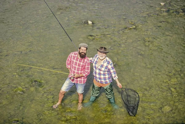 一緒に働いてる。夏の週末。成熟した男の漁師。男性の友情。家族の絆。父と息子の釣り。趣味とスポーツ活動。トラウト・ベイト。釣竿と網を持った2人の幸せな漁師が — ストック写真
