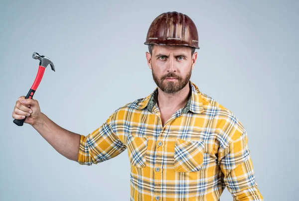 Красивый мужчина в шлеме безопасности строительства и клетчатой рубашке на строительной площадке с молотком, магазин инструментов — стоковое фото