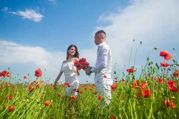 Glada par andas frisk luft i ett fält med röda vallmo blommor, romantisk dag — Stockfoto