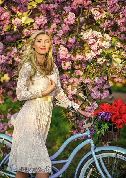 It is spring time. young fashionable girl with retro bike near cherry blossoms. girl with vintage bicycle in pink sakura alley. blooming tree in spring time. natural female beauty. woman in garden