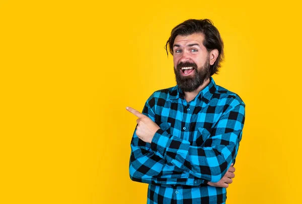 Mature man has moustache. presenting product. bearded man in checkered shirt. brutal guy with emotional face. casual male fashion look. happy handsome hipster pointing finger. barbershop. copy space — Stock Photo, Image
