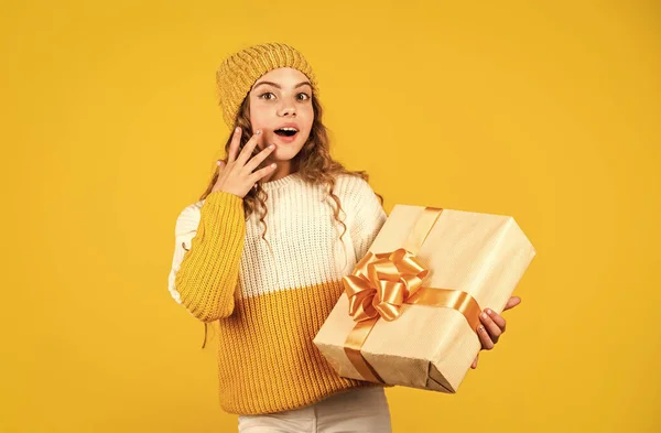 A kislány ajándékdobozt tart sárga hátterű szalaggal. A tinédzser lány ünnepi ajándékot kapott. A legjobb karácsonyi ajándékok. A gyerek izgatottan pakol ki ajándékot. Karácsonyi ajándék a lányának. Élvezd a meglepetéseket. — Stock Fotó