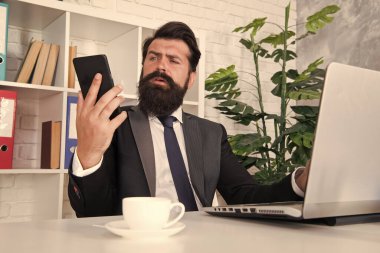 Telefon onu düzenli tutuyor. Sakallı adam telefondaki mesajları okuyor. Taşınabilir yaşam tarzı. Profesyonel kullanım için cep telefonu. İş iletişimi. Ofis hayatı. Yeni teknoloji. İletişimi koparmamak için cep telefonu