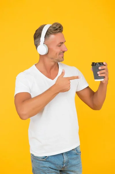 Homme non rasé écouter de la musique et index des points à emporter tasse de café promotion et publicité fond jaune, service de réalisation — Photo