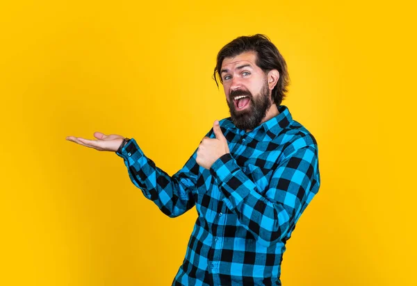 Moderno aspecto barbudo hipster presentando producto. concepto de peluquería. brutal hombre guapo con bigote. peluquero maduro sobre fondo amarillo. masculinidad y carisma. estilo de moda casual —  Fotos de Stock