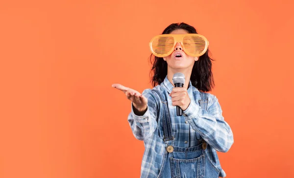 Fröhliche Dame im Hemd-Denim-Stil singt in Mikrofon auf orangefarbenem Hintergrund, Kopierraum, Stimme — Stockfoto