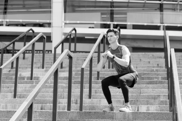 Exercício e conceito de estilo de vida saudável. homem fazendo agachamentos ao ar livre. homem com relógio fitness exercitando e fazendo agachamentos. Agachamentos profundos. jovem no sportswear fazendo agachamentos ao ar livre — Fotografia de Stock