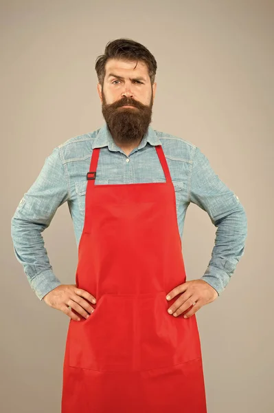 Chef barbudo ou garçom usando avental vermelho. empregado de mesa brutal ou barista. Um barbeiro de avental com barba comprida. Bonito mestre confiante. Empreendedor em seu olhar moderno — Fotografia de Stock