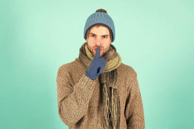 Sırrımı sakla. Tıraşsız yakışıklı adam mavi arka planda kış aksesuarları takıyor. Kış sezonu indirimi. Hippi, kış şapkası eşarbı ve eldiven ördü. Duygusal bir ifade. Gizemli bir anlaşma. Dilek listesi