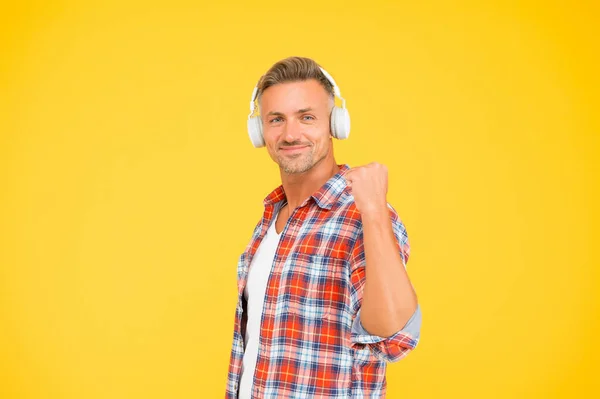 Happy man clench fist listening to music playing in modern earphones yellow background, audio — Stock Photo, Image
