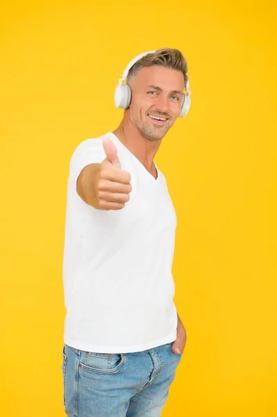 För att dina öron förtjänar det bästa. Snygg man ger tummen upp gul bakgrund. Hörlurar teknik. Godkännandemärke. Lyssnar på musik. Modern livsstil. Godkännande försäljning — Stockfoto