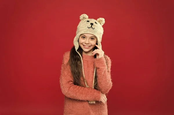 Mutluluk ve neşe. Kış kıyafeti. Küçük çocuk örgü şapka takıyor. Küçük kız kış moda aksesuarı. Küçük çocuk uzun saçlı, kırmızı arka plan takıyor. Şirin model kış tarzını seviyor. Sevimli küçük ayı. — Stok fotoğraf
