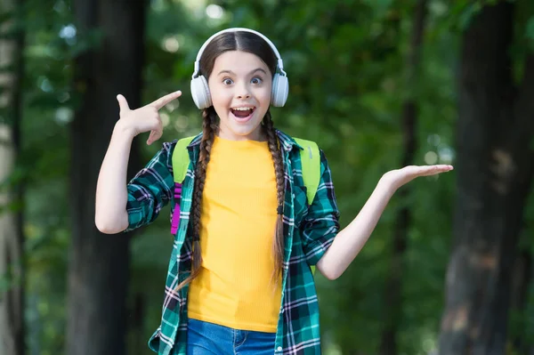 Szczęśliwy dzieciak wskazuje palcem na nowoczesne słuchawki trzymając otwartą rękę, prezentując produkt, przestrzeń do kopiowania — Zdjęcie stockowe