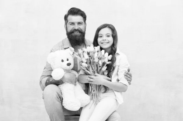 Feliz dia das mulheres. A família feliz celebra o dia de mulheres. Homem barbudo e criança pequena segurar flores e brinquedo. Pai e filha pequena. Férias. 8 de março celebração. Férias internacionais de mulheres — Fotografia de Stock