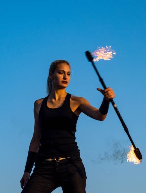 Şehvetli kadın ateş manipülatörü alevli baton çeviriyor. Açık havada mavi gökyüzü, tehlikeli.