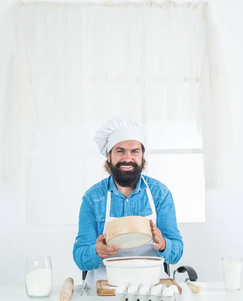 I love my job. mature bearded man wear chef hat using sieve. male cook preparing food in home kitchen. brutal hipster in apron cooking meal. time for eating. happy baking. concept of housekeeping