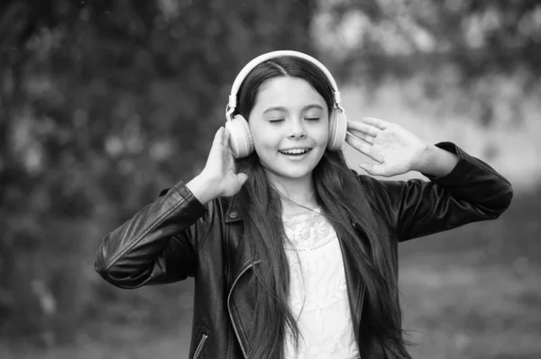 Słucha muzyki. Szczęśliwe dziecko nosi słuchawki na zewnątrz. Mała dziewczynka słucha muzyki w słuchawkach. Wygodne nauszniki. Urządzenia zabezpieczające uszy. Ochrona słuchu. Nowa technologia. Współczesne życie — Zdjęcie stockowe