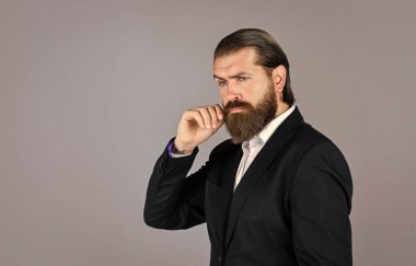 Ciddi sakallı iş adamı. Modern görünümlü şık, olgun bir adam. Erkek ceketi dolabı. Takım elbiseli şık bir adam. Resmi manken. Gri arka planda duran yakışıklı adam. Boşluğu kopyala