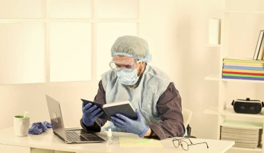 Kitabı oku. Adam solunum maskesi, eldiven ve koruyucu gözlük takıyor. Evde güvende kal. Koronavirüs salgını. Hijyen kilitlendi. uzaktan çalışma konsepti. Sıhhi doktor üniformalı bir adam.